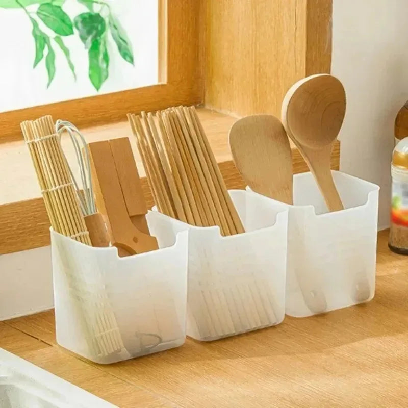 Set of wooden utensils in a white caddy on a wooden surface with a window in the background.